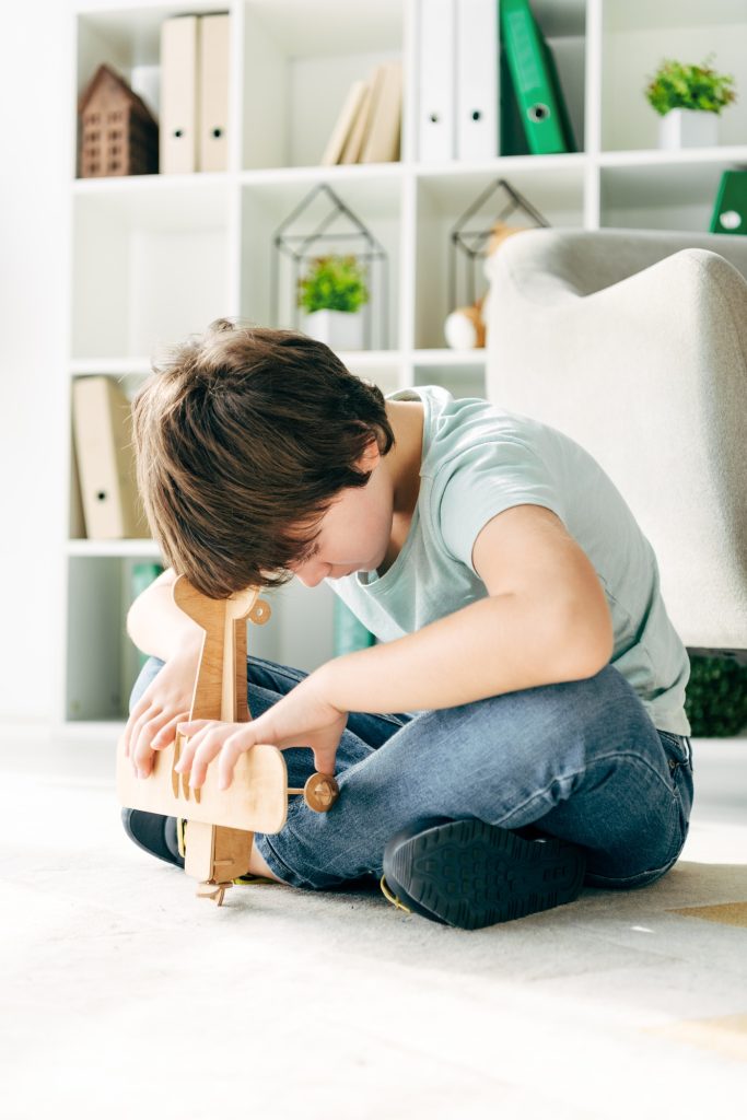 kid with dyslexia sitting on floor and holding wooden plane